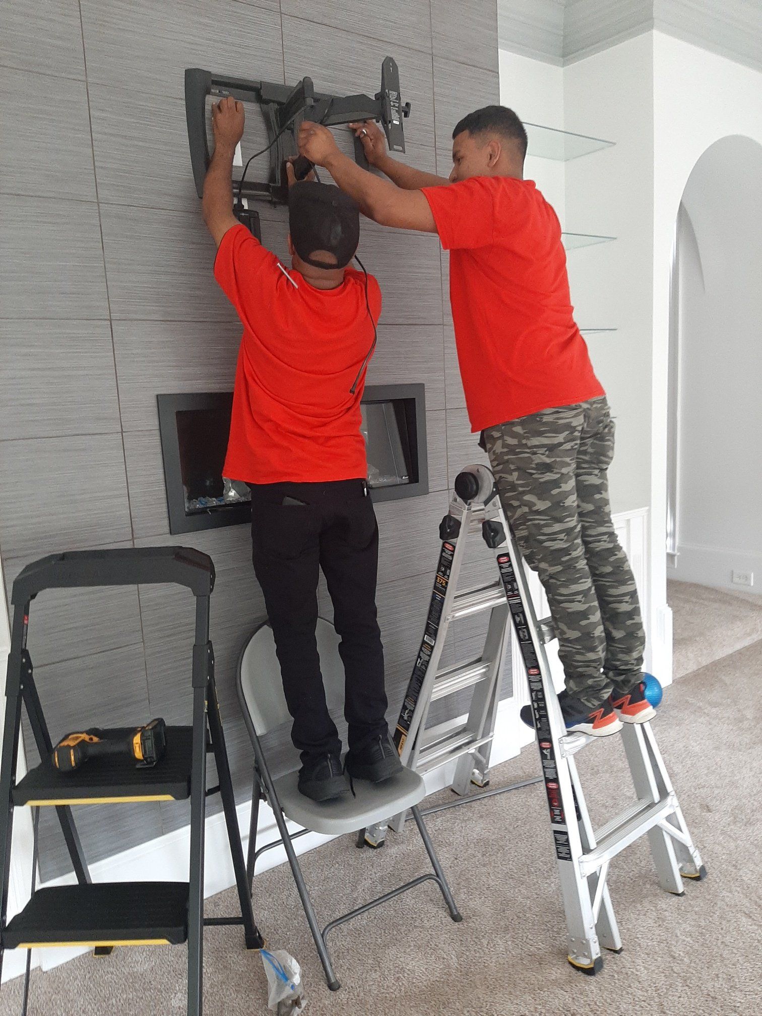 Two men are working on a tv mount on a wall.