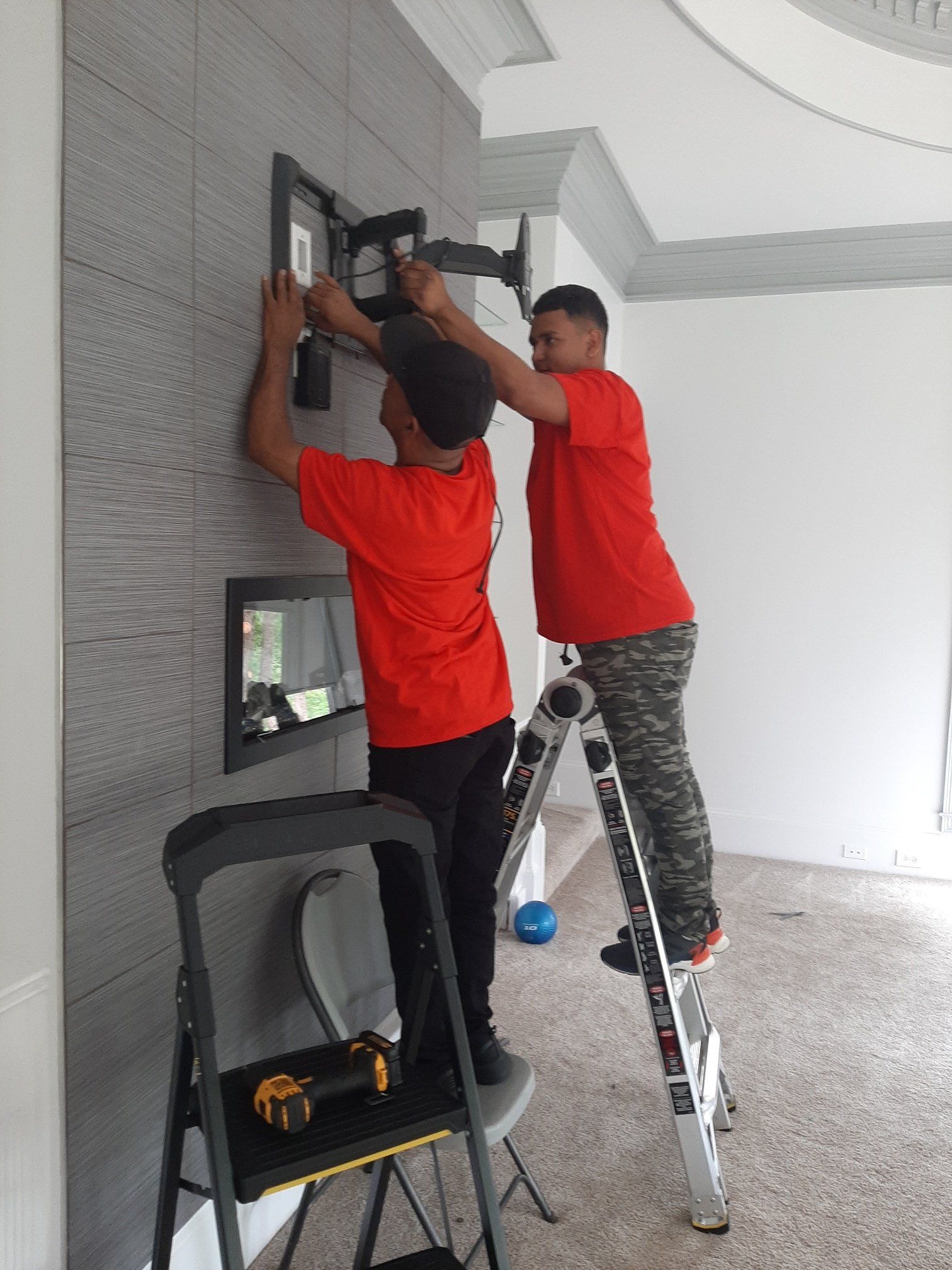 Two men are working on a tv mount on a wall.