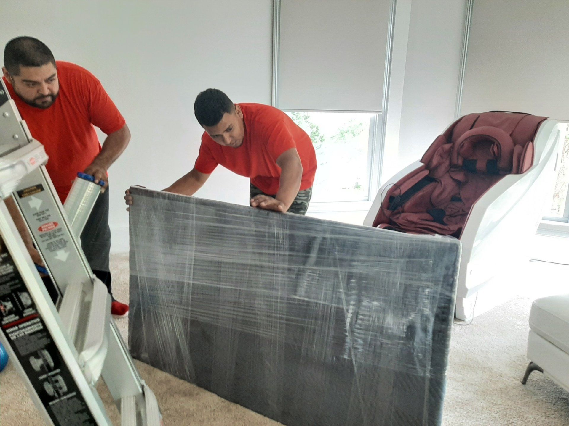 Two men are wrapping a television in plastic wrap in a living room.