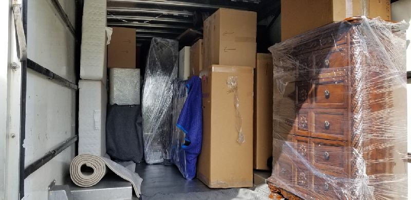 The inside of a moving truck filled with boxes and a dresser.