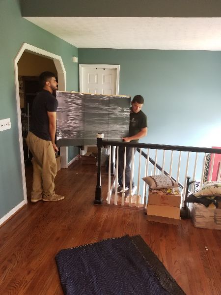 Two men are carrying a large piece of furniture in a living room.