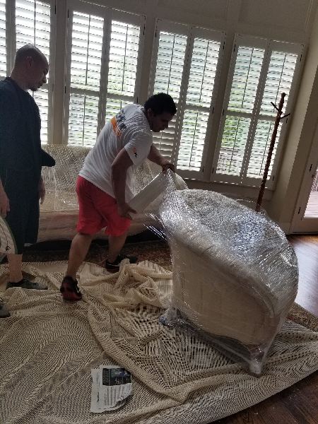 A man is wrapping a chair in plastic wrap in a living room.