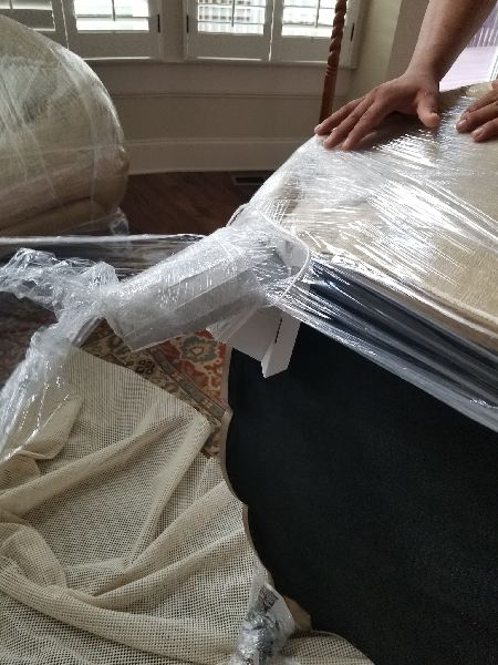 A person is wrapping a piece of furniture in plastic wrap.