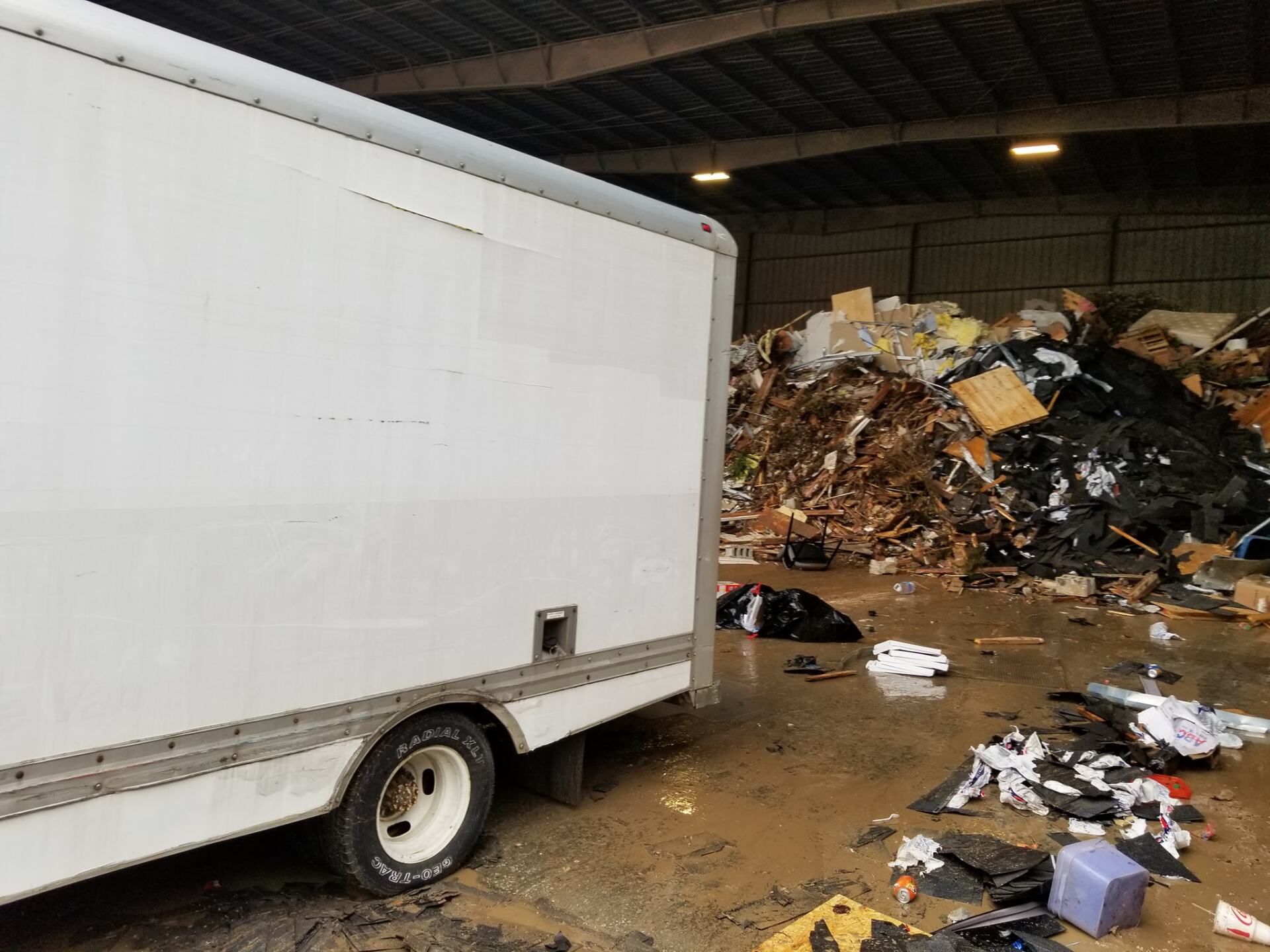 A white truck is parked in a warehouse next to a pile of trash.