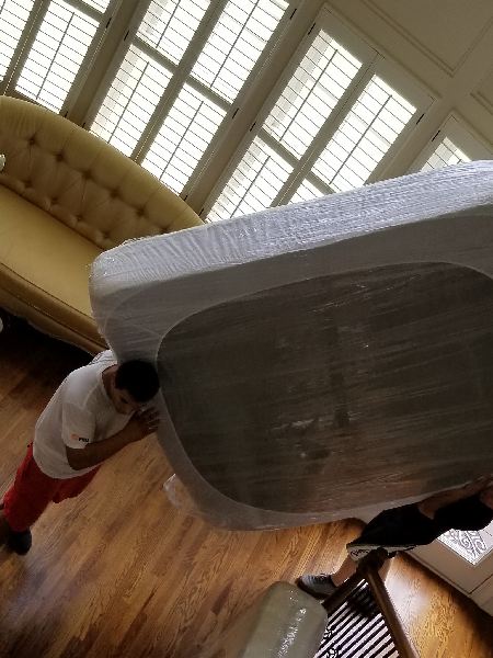A man is carrying a mattress in a living room.