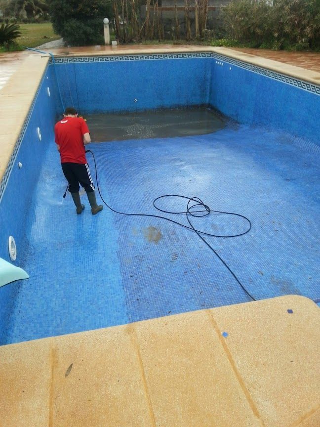 A man in a red shirt is cleaning a swimming pool with a hose
