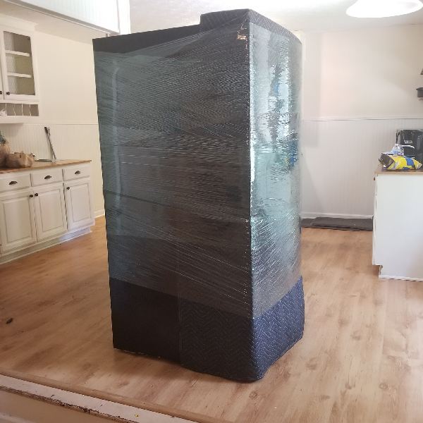 A refrigerator is wrapped in plastic in a kitchen.