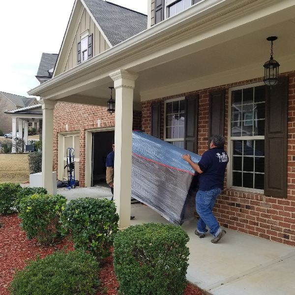 A man is carrying a large piece of furniture in front of a brick house