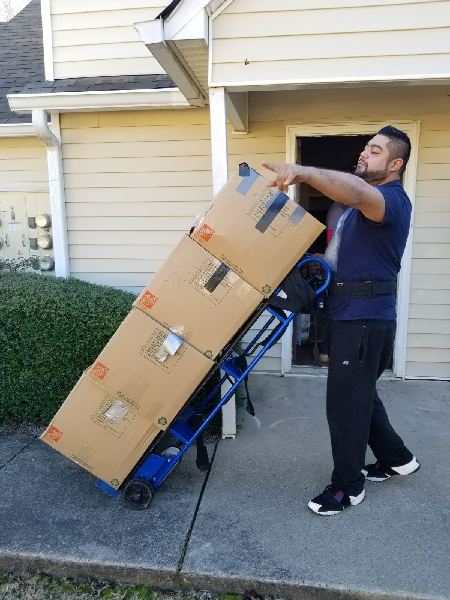 A man is pushing a cart with boxes on it in front of a house.