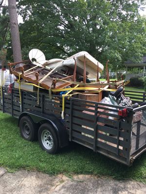 A trailer filled with junk is parked in the grass.