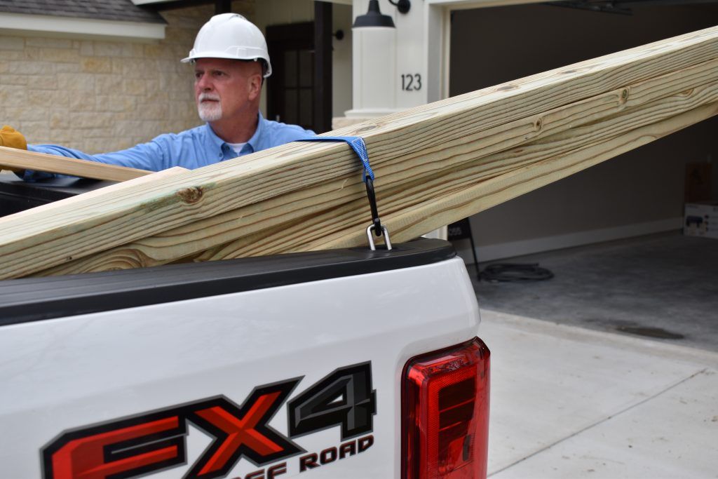 A man is carrying a stack of wood in the back of a truck.
