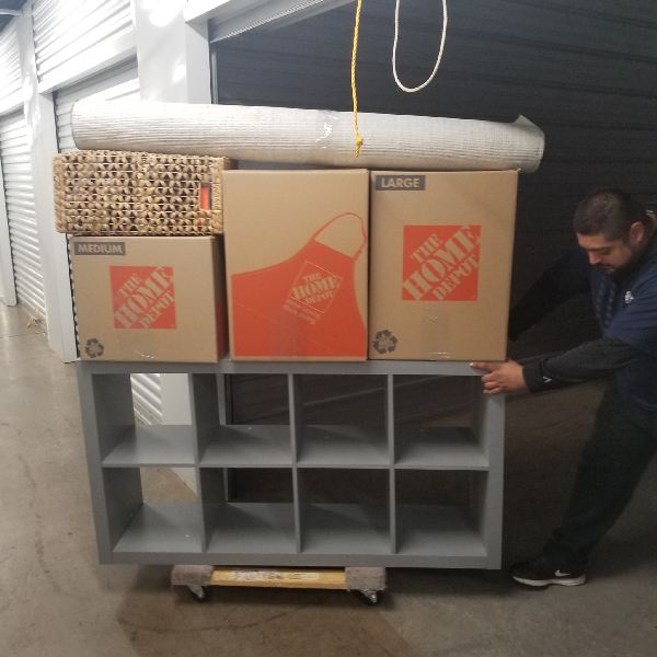 A man is pushing a shelf with boxes from the home depot on top of it