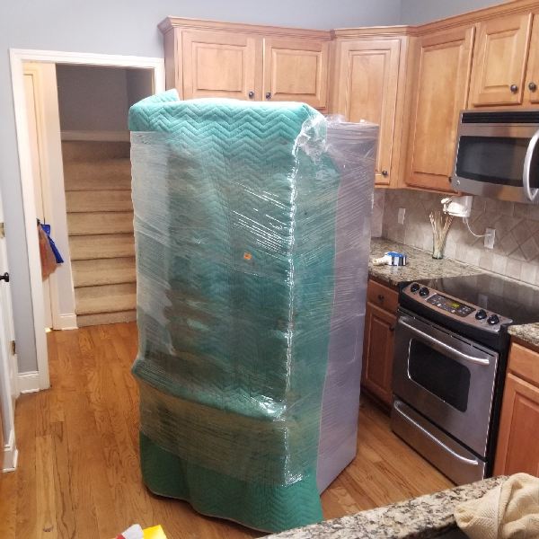A refrigerator is wrapped in green plastic in a kitchen