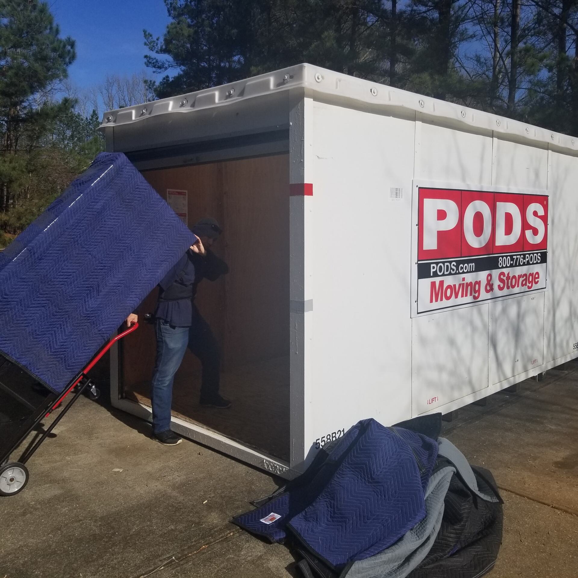 A man is pushing a blue blanket into a pods moving and storage trailer