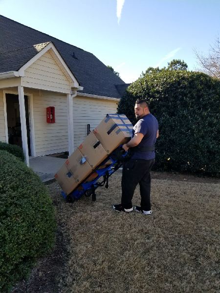 A man is pushing a cart with boxes on it in front of a house