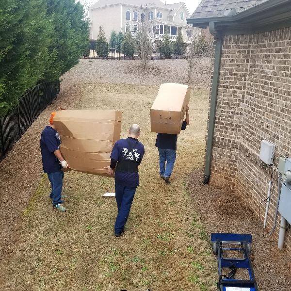 Three men are carrying boxes in front of a brick house
