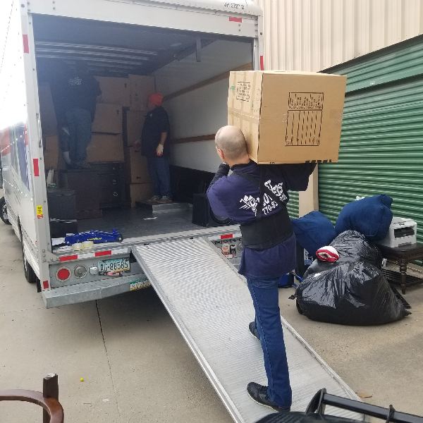 A man is carrying a cardboard box that says ' moving company ' on it