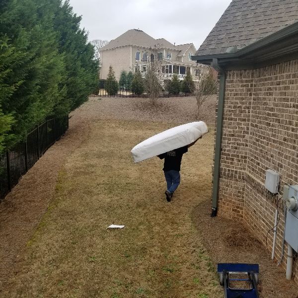 A man is carrying a mattress in his backyard.