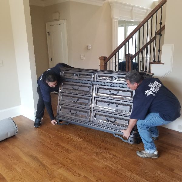 Two men are moving a large dresser in a living room.