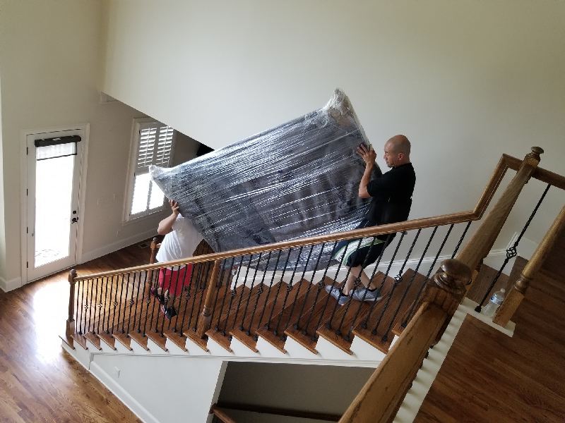 Two men are carrying a mattress up a set of stairs.