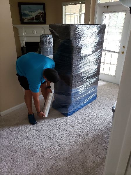 A man is wrapping a couch in plastic wrap in a living room.