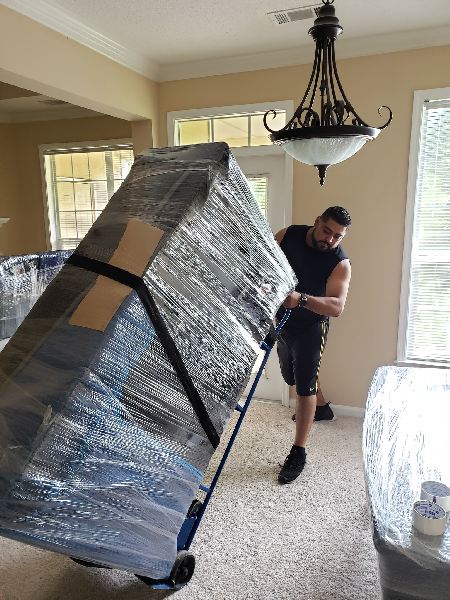 A man is pushing a large box on a dolly in a living room.