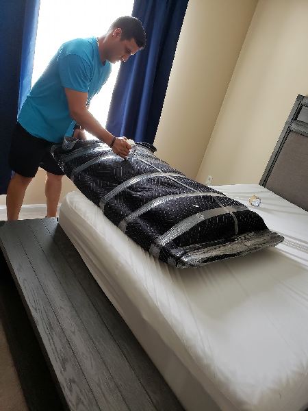 A man in a blue shirt is making a bed in a bedroom.