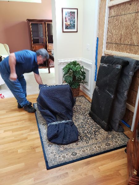 A man is wrapping a chair with a blue blanket in a living room