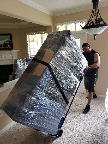 A man is carrying a large piece of furniture on a dolly.