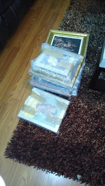 A stack of pictures sitting on top of a rug on a wooden floor.