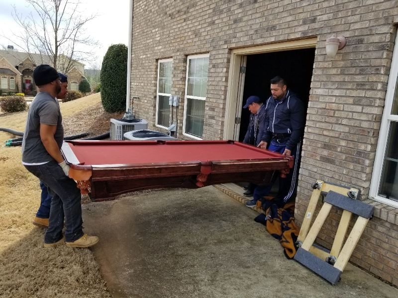 A group of men are carrying a pool table out of a garage.