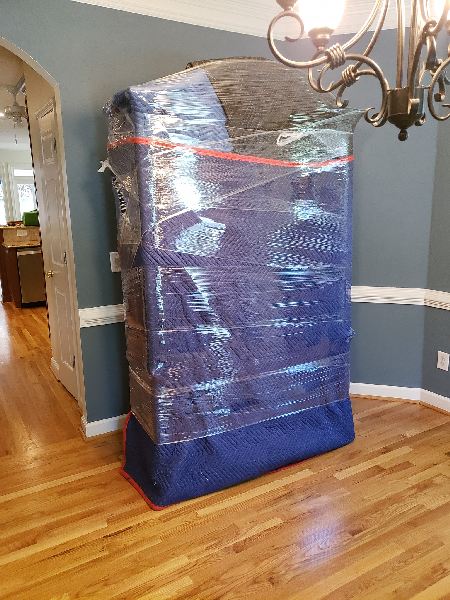 A large piece of furniture is wrapped in plastic in a dining room.