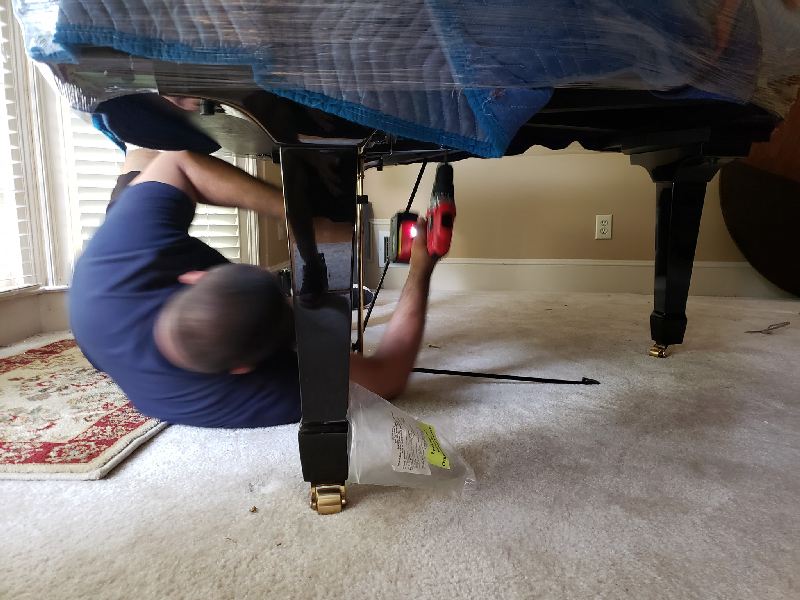A man laying on the floor working on a piano
