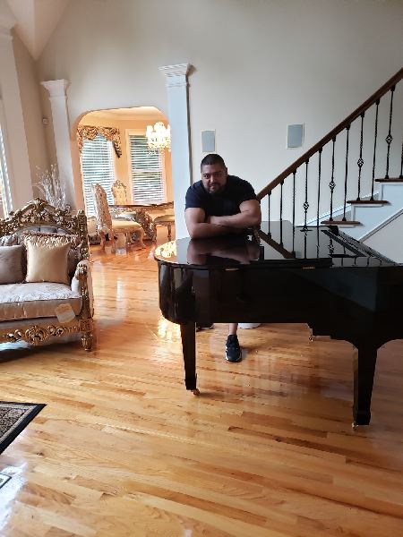 A man is sitting at a piano in a living room next to a staircase.