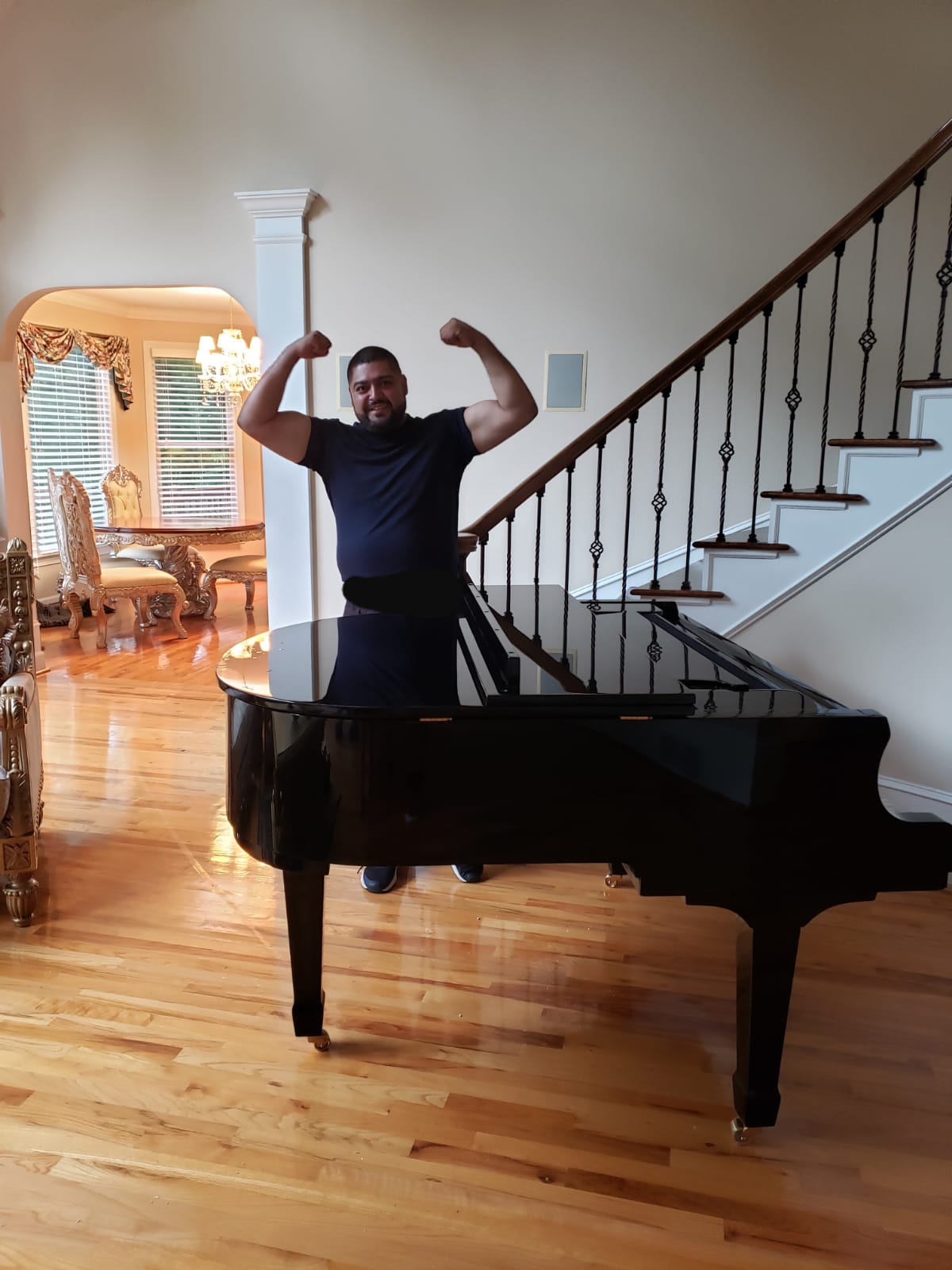 A man is flexing his muscles in front of a piano in a living room.