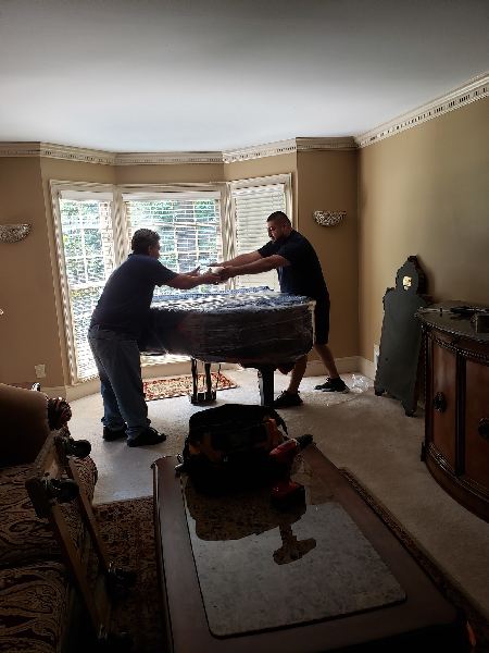 Two men are moving a piano in a living room.