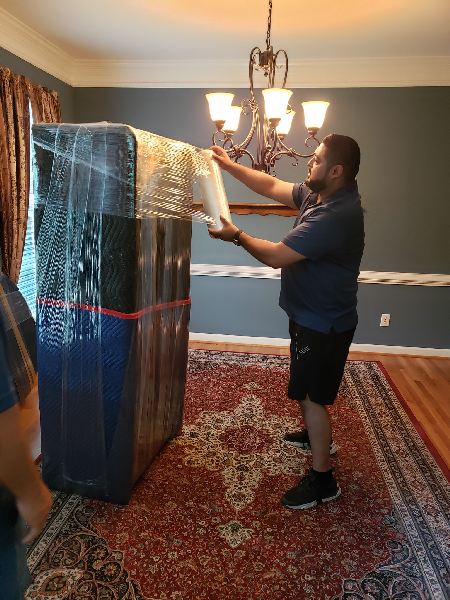 A man is wrapping a couch in plastic wrap in a dining room.