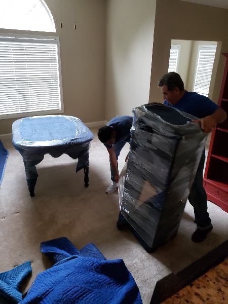 Two men are moving a stack of furniture in a living room.