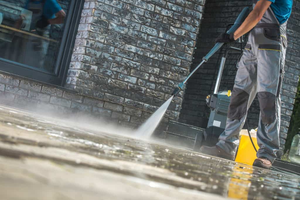 A man is cleaning the sidewalk with a high pressure washer.