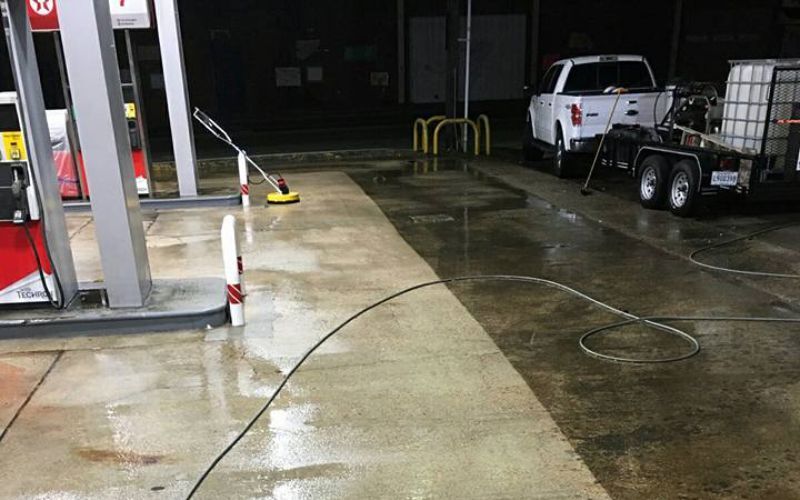 A gas station is being cleaned at night with a truck parked in the background.
