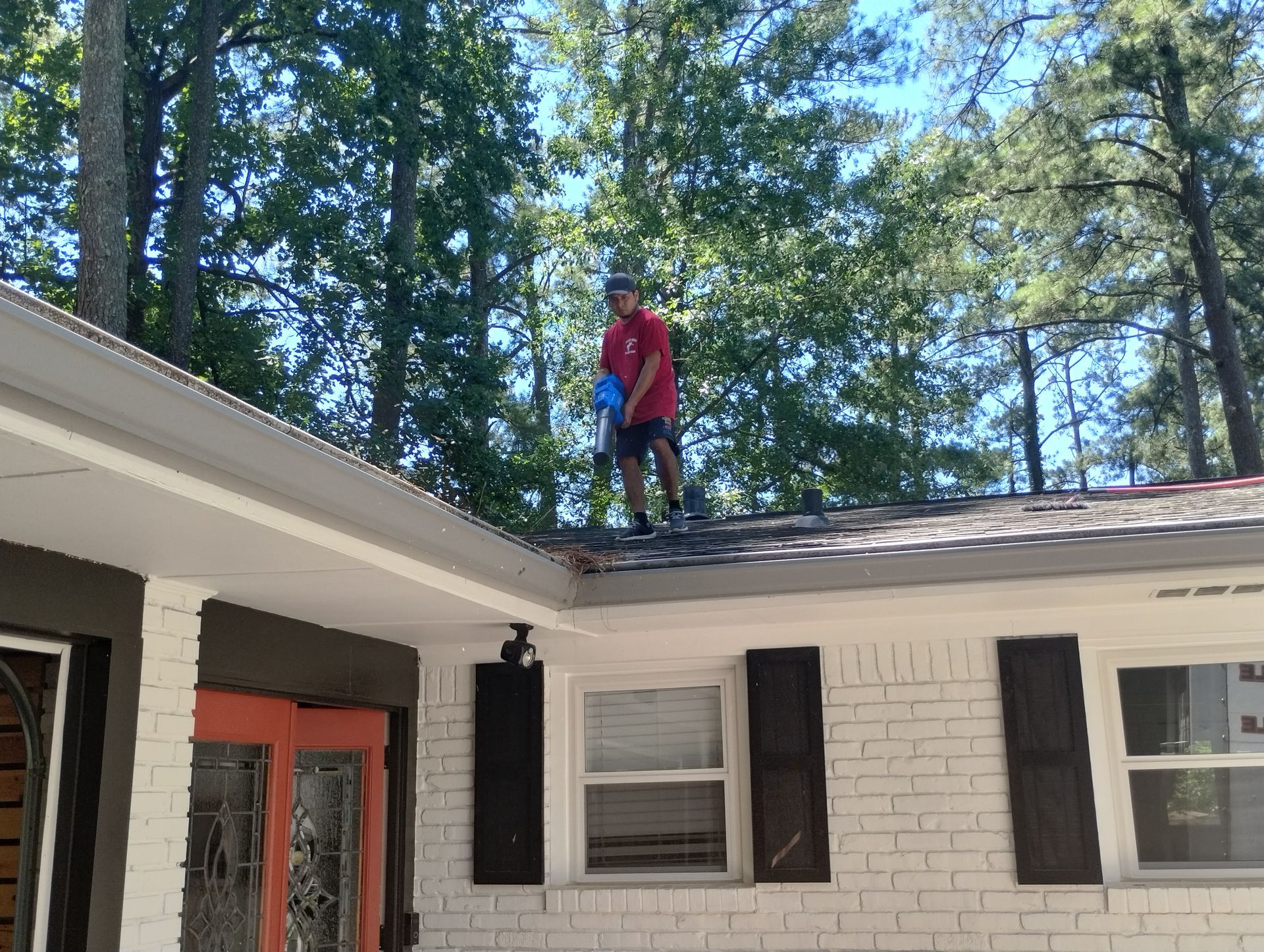 A man in a red shirt is standing on the roof of a house.
