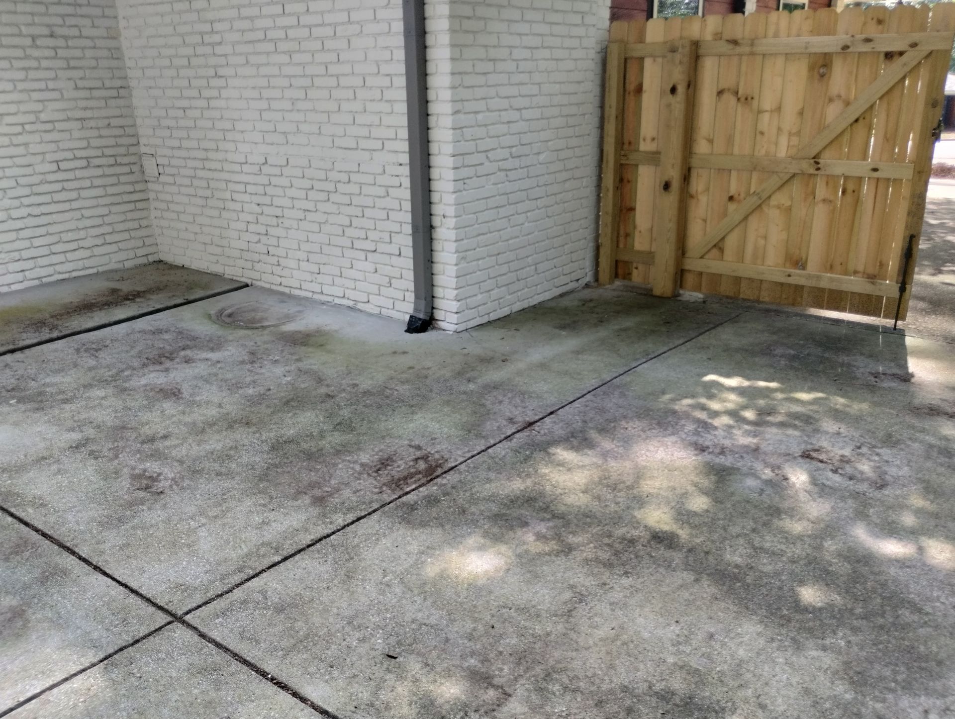 A concrete driveway with a wooden gate and a white brick wall.