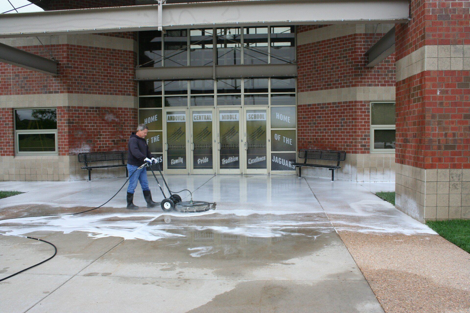 A man is cleaning the sidewalk in front of a brick building