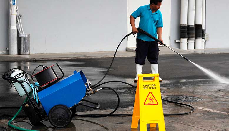 A man is using a high pressure washer to clean a caution sign