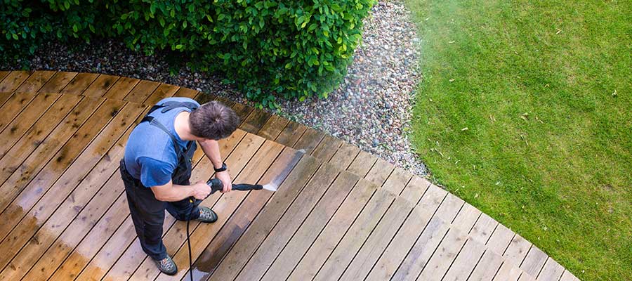 A man is cleaning a wooden deck with a high pressure washer.