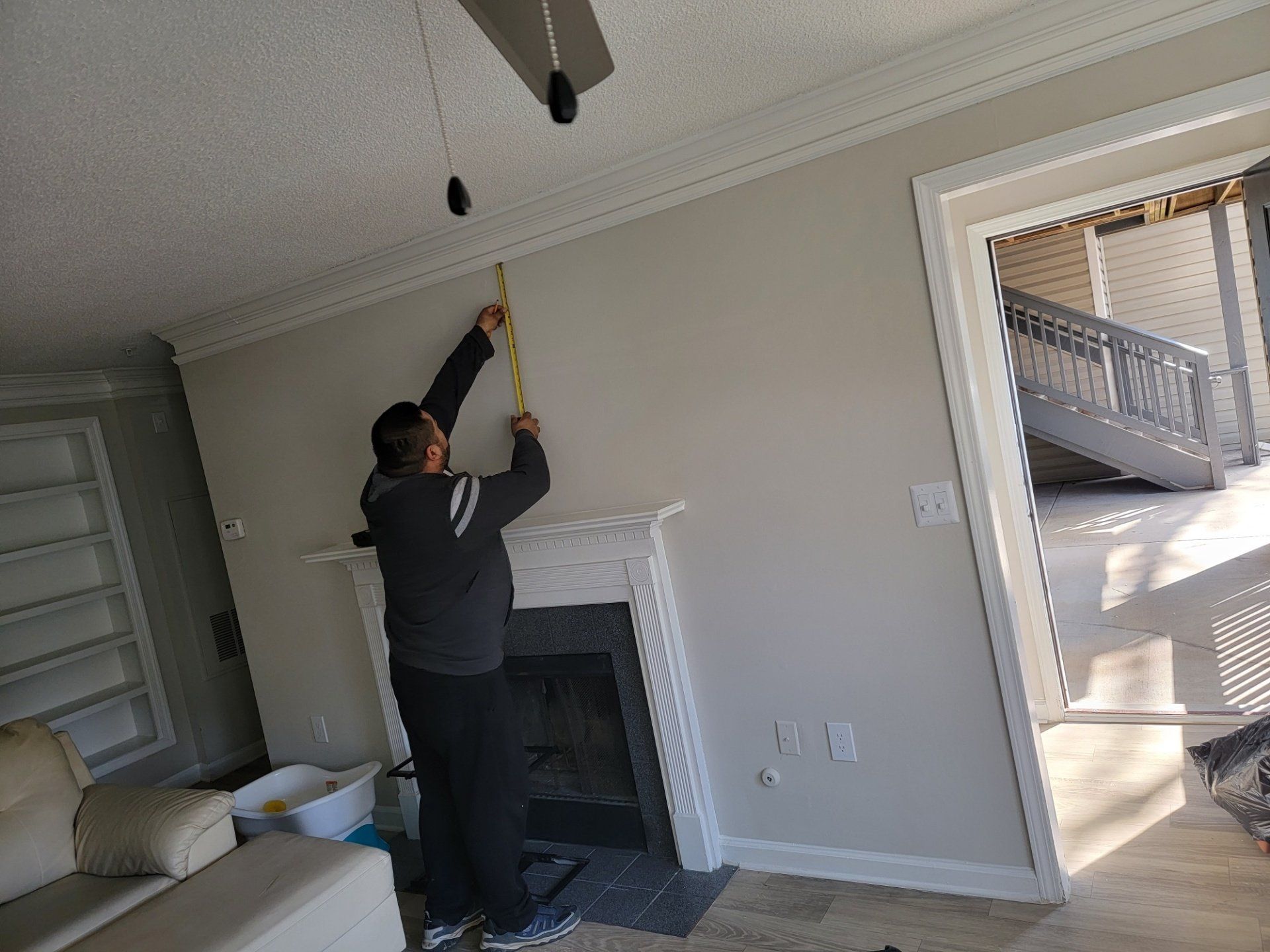 A man is measuring a fireplace with a tape measure in a living room.
