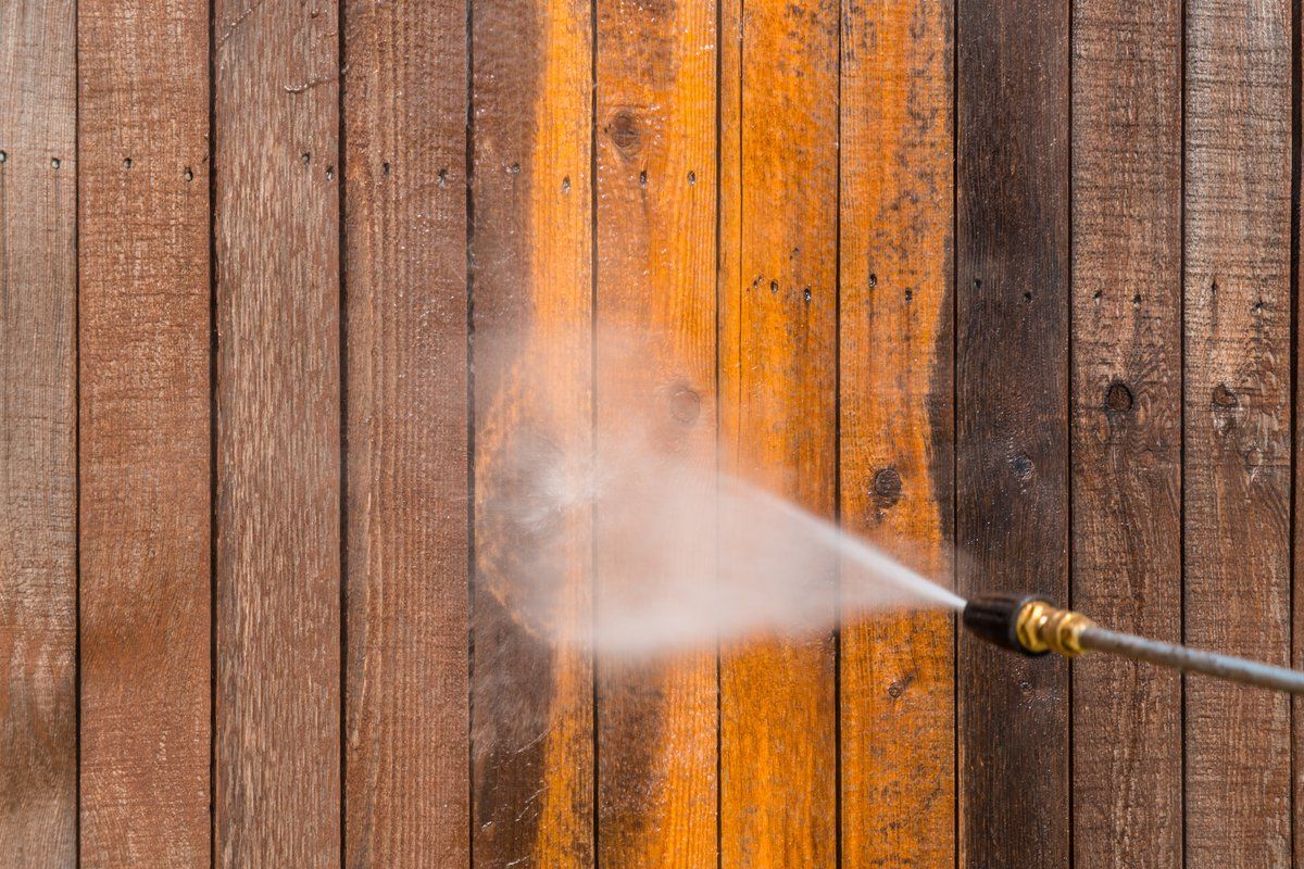 A person is using a high pressure washer to clean a wooden fence.