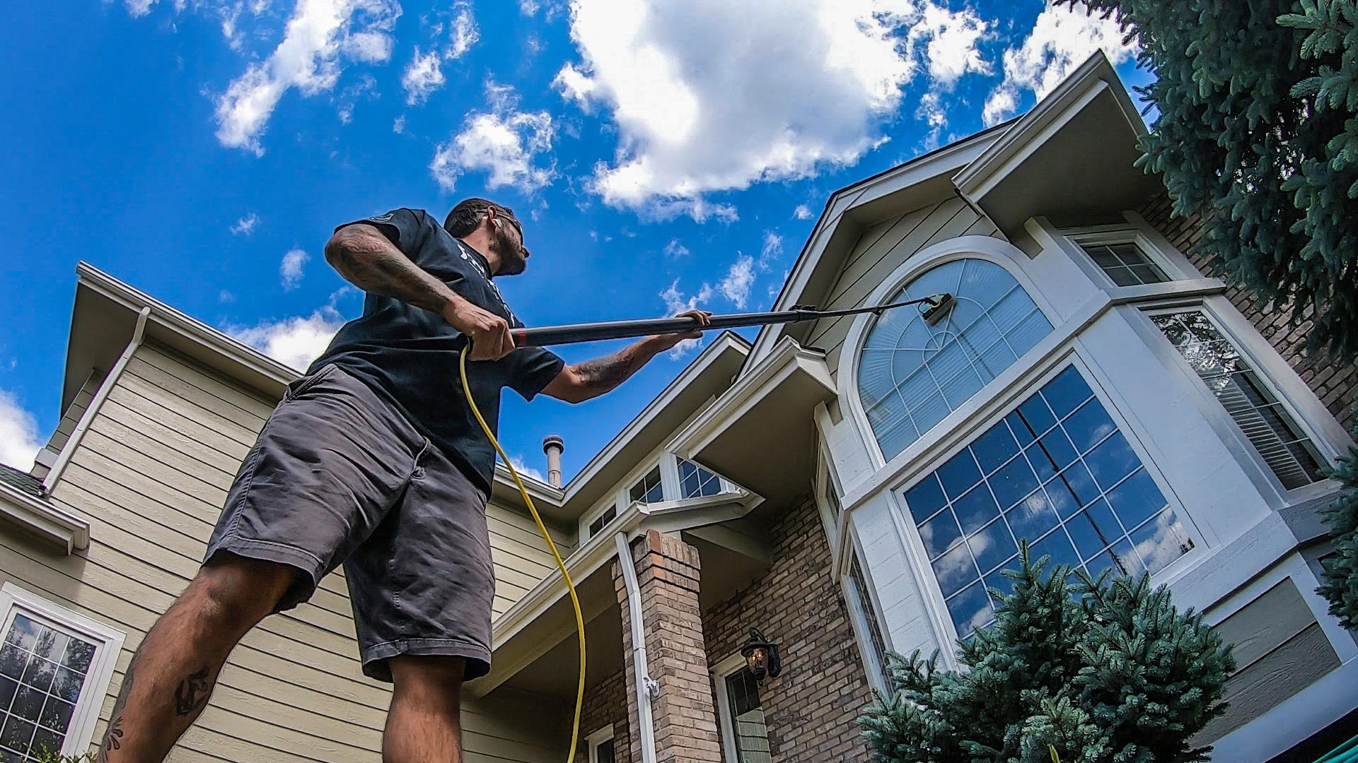 A man is cleaning the roof of a house with a high pressure washer.