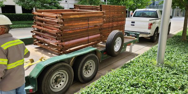 A man is standing next to a trailer filled with wooden scaffolding.