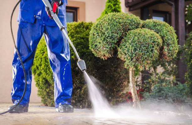 A man is using a high pressure washer to clean a sidewalk in front of a house.